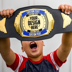 May include: A black and gold championship belt with a blue ribbon and the text "CUSTOM TEXT CUSTOM TEXT YOUR DESIGN HERE CUSTOM TEXT CUSTOM TEXT".