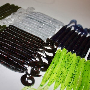 May include: Assortment of fishing lures in various colors, including green, black, white, and blue. The lures are made of soft plastic and have a worm-like shape.