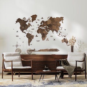 May include: A wooden world map wall decor with a light brown finish. The map is made of individual pieces of wood that are assembled to form the continents. The map is mounted on a white wall and is surrounded by two armchairs and a coffee table. The map includes the names of some of the continents and oceans.