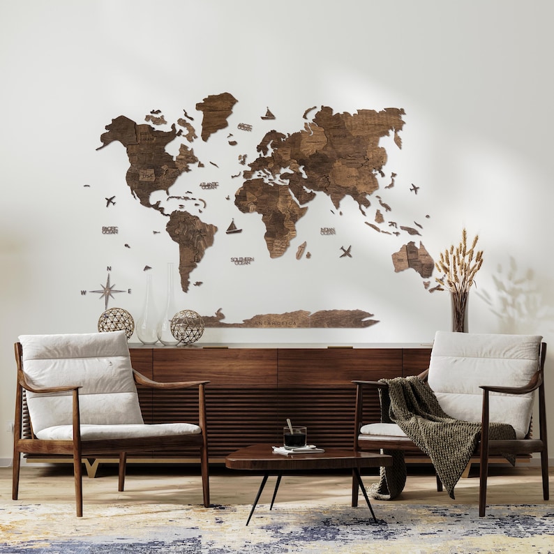 May include: A wooden world map wall decor with a light brown finish. The map is made of individual pieces of wood that are assembled to form the continents. The map is mounted on a white wall and is surrounded by two armchairs and a coffee table. The map includes the names of some of the continents and oceans.