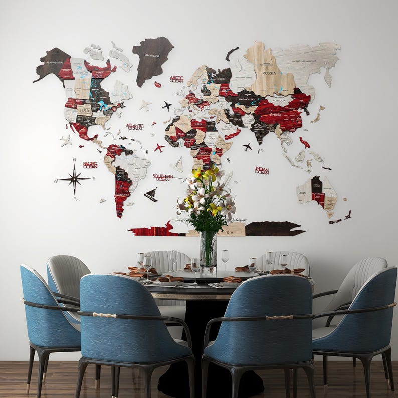 May include: A wooden world map in various colours, mounted on a white wall. A dining table with blue chairs and a vase of flowers is in front of the map. The map includes country names.