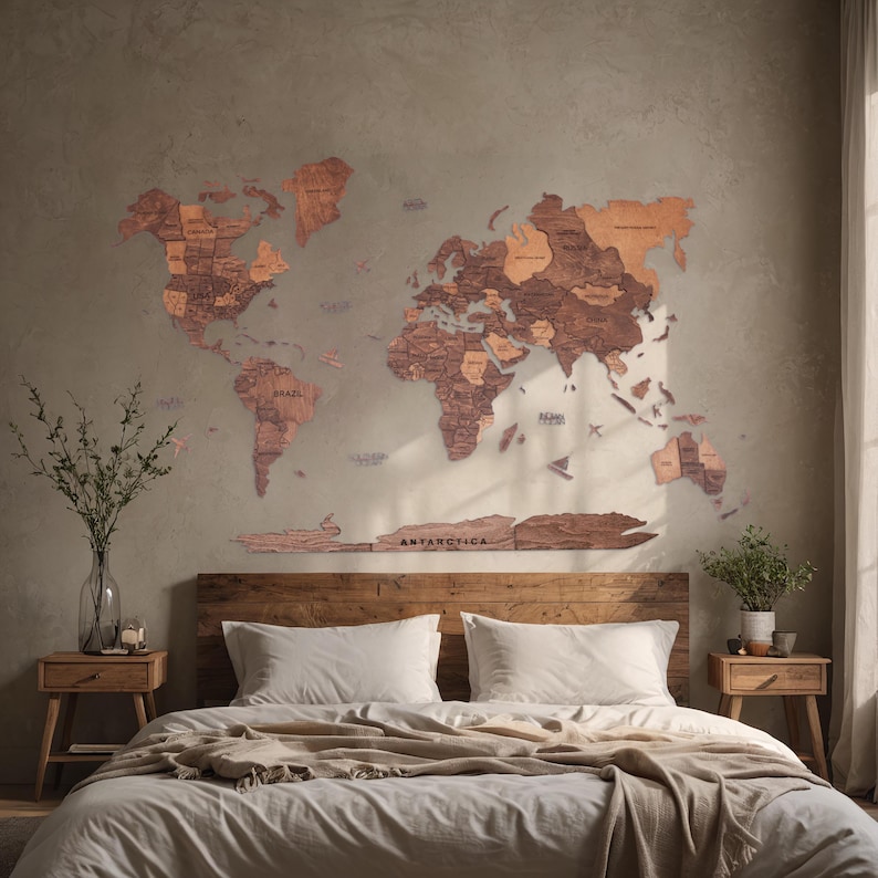 May include: A wooden world map with a light brown finish is mounted on a wall above a bed with white bedding and a brown throw blanket. The map is made up of individual pieces of wood that fit together to form the continents. The map includes the text "ANTARCTICA".