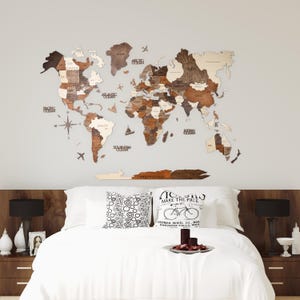 May include: A wooden world map in brown and beige tones is displayed above a bed. The map features country names and ocean labels. The bed has white bedding, decorative pillows, and dark wood bedside tables with lamps.
