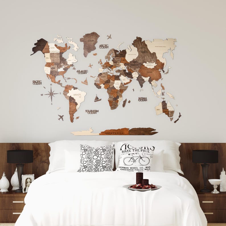 May include: A wooden world map in brown and beige tones is displayed above a bed. The map features country names and ocean labels. The bed has white bedding, decorative pillows, and dark wood bedside tables with lamps.