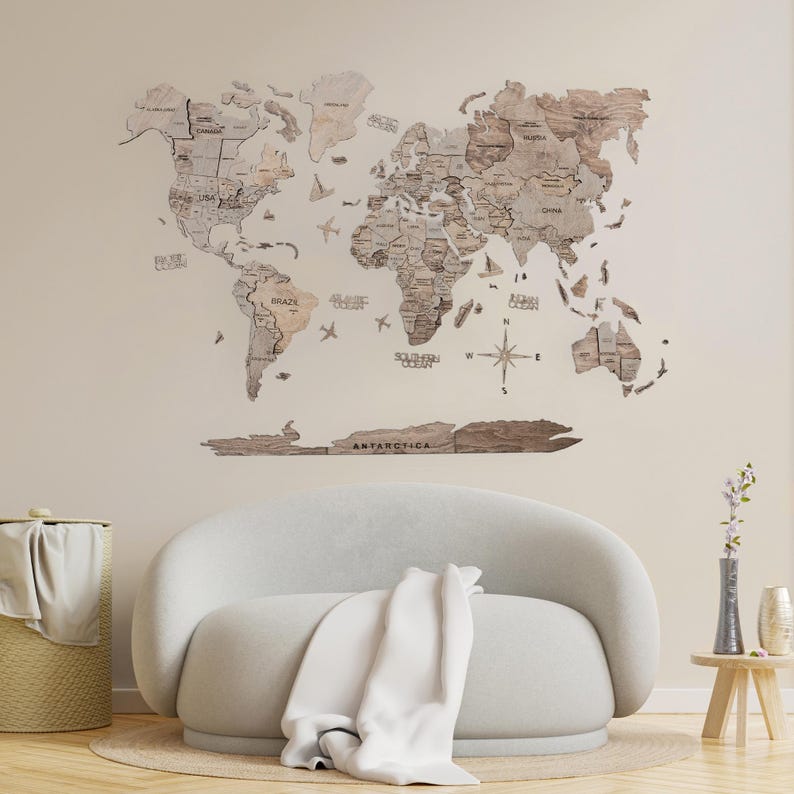 May include: A wooden world map with a compass and airplane cutouts. The map is mounted on a light beige wall above a white sofa with a white throw blanket.