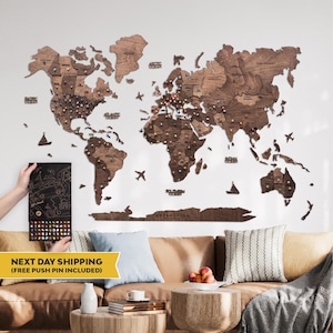 May include: A large, multi-piece wooden world map wall art installation featuring dark brown wood grain, engraved country names, and ocean labels. The map includes decorative wooden airplane and sailboat icons, with numerous colorful push pins inserted.