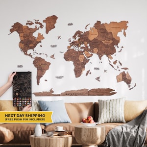 May include: A large wooden world map wall art piece featuring various shades of brown wood, with laser-cut continents and country names. The map includes decorative wooden icons of airplanes and ships, and is displayed with a box of colorful push pins.