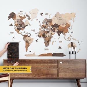 May include: A large wooden world map wall art installation featuring various shades of brown and beige wood tones. The map includes labeled continents and countries, decorative wooden icons of ships and planes, and a black box of push pins.