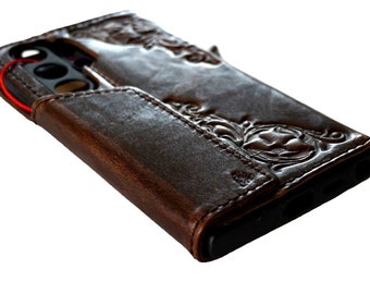 May include: A brown leather phone case with an intricate floral design. The case has a flap that covers the phone's screen and a slot for cards.