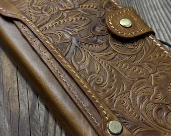 May include: A brown leather wallet with a floral embossed design. The wallet features a snap closure and visible stitching. The leather has a distressed appearance, with a vintage aesthetic.