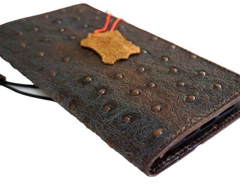 Könnte beinhalten: Eine braune Leder-Handyhülle mit einem strukturierten Straußenledermuster und einem kleinen Lederanhänger. Die Hülle hat eine Klappe, die über das Handy geklappt wird.