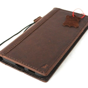 May include: A brown leather phone case with a strap. The case has a stitched edge and a small leather tag attached.