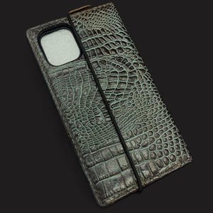 May include: A green crocodile-embossed leather phone case with a black elastic band closure.