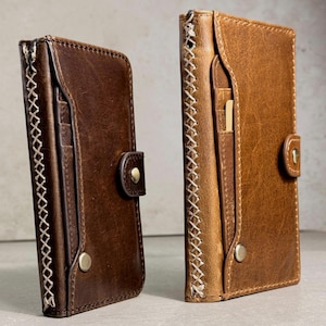 Op de afbeelding: Twee bruine leren portemonnees met zichtbare stiksels en knoopsluitingen. De portemonnees hebben kaartsleuven en een klassiek ontwerp. Het leer heeft een verweerde uitstraling, wat bijdraagt aan de rustieke esthetiek.