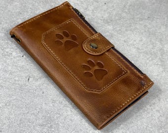 Peut inclure: Un portefeuille en cuir marron avec un motif de pattes de chien. Le portefeuille a une fermeture à bouton-pression et une fermeture éclair. Le portefeuille est rectangulaire.