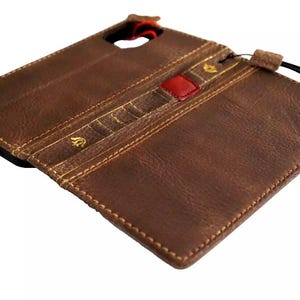 Könnte beinhalten: Eine braune Leder-Handyhülle mit roten und goldenen Akzenten. Die Hülle hat eine Klappe, die mit einem Druckknopf geschlossen wird.