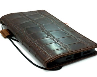 Peut inclure: Une coque de téléphone en cuir marron avec un motif gaufré en crocodile. La coque a une sangle noire et un téléphone noir à l'intérieur.
