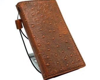 Könnte beinhalten: Ein braunes Leder-Notizbuchcover mit einem Straußenledermuster. Das Cover hat einen schwarzen Gummibandverschluss und eine kleine braune Lederschlaufe.