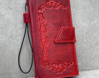 Könnte beinhalten: Eine rote Leder-Handyhülle mit geprägtem floralem Design und einer Handschlaufe. Die Hülle hat einen Magnetverschluss. Die Hülle ist etwa 15 cm hoch und 7,6 cm breit.
