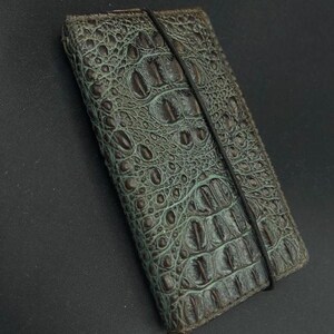May include: A dark green leather wallet with a crocodile pattern and a black elastic band closure.