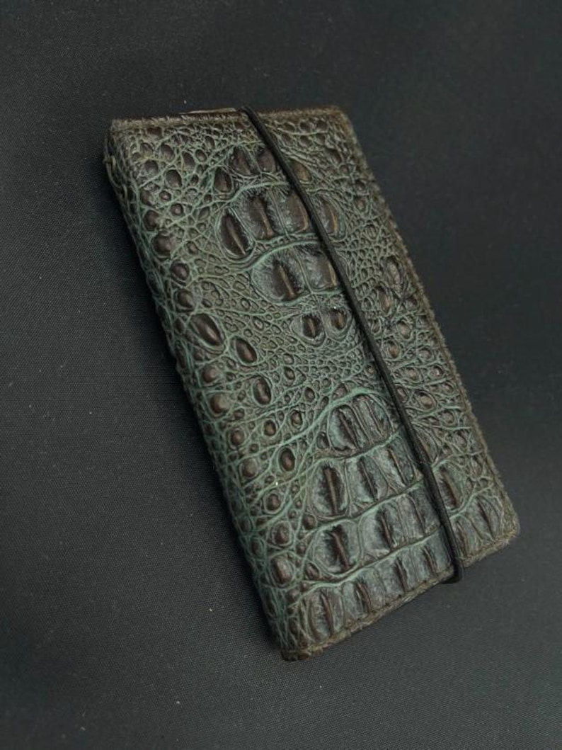 May include: A dark green leather wallet with a crocodile pattern and a black elastic band closure.