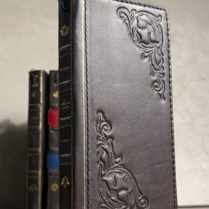 May include: A dark brown leather-bound book featuring embossed floral corner patterns on the front cover. The spine displays gold-colored vertical lines, a small emblem, and the text "BOOK", "davis", "cate", and "-1968-" printed in a serif font.