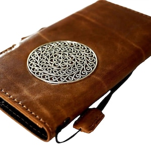 May include: A brown leather wallet with a silver filigree design on the front. The wallet has a flap closure and a black strap.