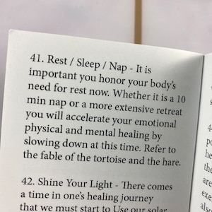 Puede incluir: Libro abierto con texto sobre descanso, sue&ntilde;o y siestas, enfatizando la importancia de honrar la necesidad de descanso del cuerpo. El texto tambi&eacute;n menciona la curaci&oacute;n emocional, f&iacute;sica y mental.