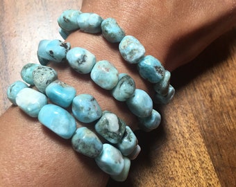 May include: Four turquoise blue gemstone bracelets stacked on a person's wrist. The bracelets are made of smooth, rounded stones.