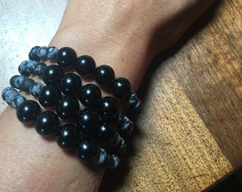 May include: A stack of bracelets with black and white beads. The bracelets are worn on a person's wrist.
