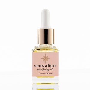May include: A small glass bottle with a gold cap and dropper filled with a yellow liquid. The label is pink with a gold star and the text "stars align™ manifesting oils Dreamcatcher".