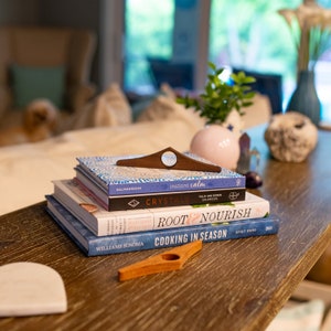 May include: A stack of four books on a wooden table. The books are titled "Instant Calm", "Crystals", "Root & Nourish", and "Cooking in Season".