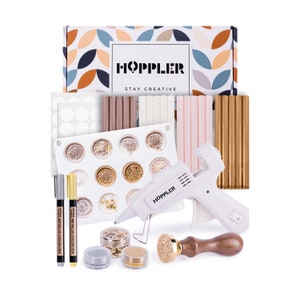May include: A craft kit with a white glue gun, wax sticks in gold, pink, white, and brown, a silicone mold, two metallic color pens, and a wooden stamp with a gold metal top. The kit is packaged in a box with the text "HOPPLER STAY CREATIVE".