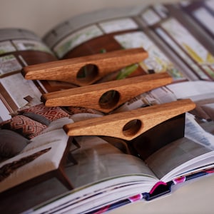 May include: Three wooden bookends in the shape of a boat with a hole in the center. The bookends are made of a light brown wood and are sitting on top of a book.