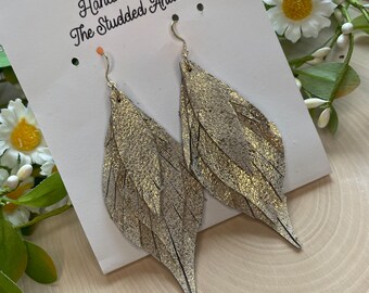 May include: Gold leather feather earrings with a gold hook. The earrings are handmade by The Studded Antler.