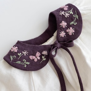 May include: A dark purple collar with embroidered pink flowers and green leaves. The collar is tied with a matching purple ribbon. The collar is on a white background.