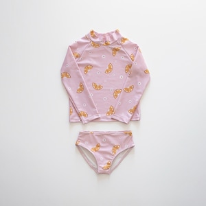 May include: A light pink two-piece swimsuit set, comprising a long-sleeved top and matching bottoms. The set is patterned with orange slices and small white flowers. The top has a high neckline. The swimsuit is designed for swimming.