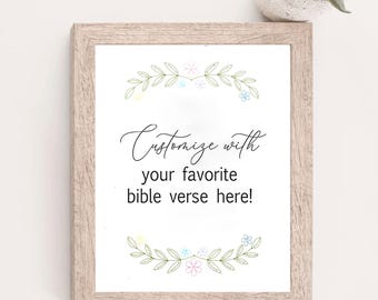 May include: A rectangular light wood frame containing a white print with the black text Customize with your favorite bible verse here! The text is surrounded by two symmetrical green leafy vine borders with small pastel-colored flowers.