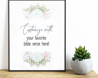 May include: A framed print featuring the black text "Customize with your favorite bible verse here!" centered between two floral illustrations. The flowers are outlined in green, blue, and pink. The frame is thin and black.