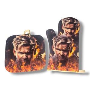 May include: A black oven mitt and pot holder set featuring a portrait of a man with blonde hair and a stern expression, set against a fiery background. The pot holder has a loop for hanging.
