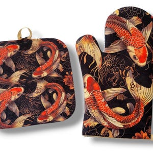 May include: A black oven mitt and pot holder set featuring a koi fish design. The fish are red, orange, and white, with detailed fins and scales. The background is black with gold accents and floral patterns. The pot holder has a gold loop.