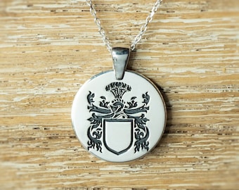 May include: Silver pendant necklace with a round, engraved charm featuring a heraldic crest with a shield and floral designs.