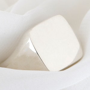 Puede incluir: Un anillo de sello de plata con una cara cuadrada.