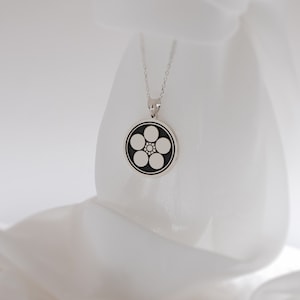 May include: A silver necklace with a round pendant featuring a black and white five-pointed flower design.