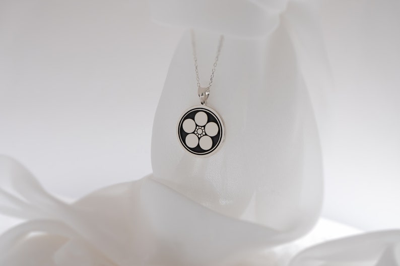 May include: A silver necklace with a round pendant featuring a black and white five-pointed flower design.