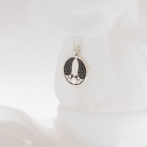 May include: A silver necklace with a round pendant featuring a black and white design of two birds with outstretched wings.