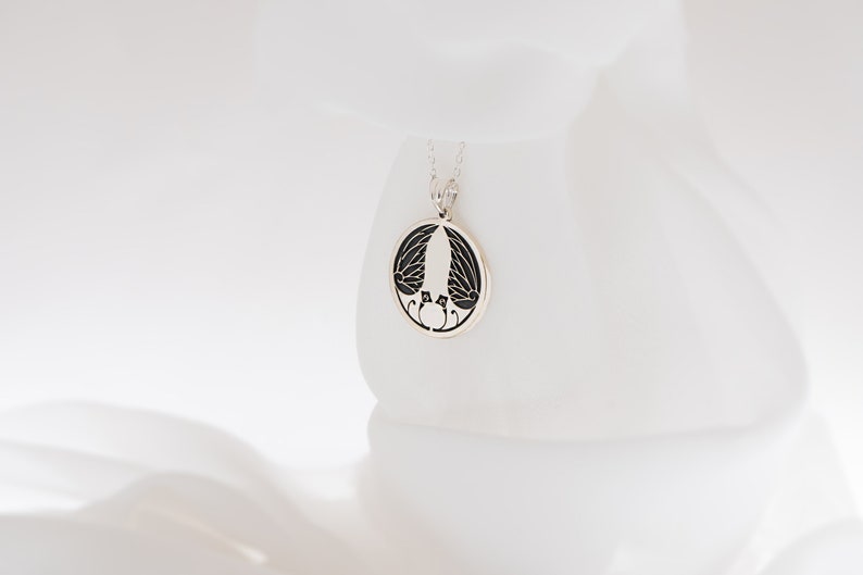 May include: A silver necklace with a round pendant featuring a black and white design of two birds with outstretched wings.
