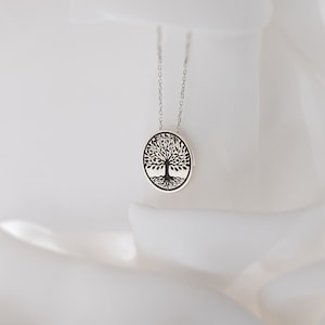 May include: A silver necklace with a round pendant featuring a black tree of life design.