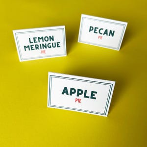 Puede incluir: Tres tarjetas rectangulares blancas con bordes verdes y texto sobre un fondo amarillo. Las tarjetas dicen "LEMON MERINGUE PIE", "PECAN PIE" y "APPLE PIE" en fuentes verde oscuro y rojo.