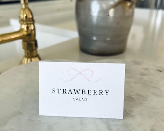 May include: A white card with a pink ribbon design and the text "STRAWBERRY SALAD" printed in black.